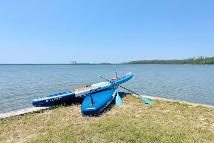 Two inflatable stand-up paddleboards with paddles rest on a grassy bank next to a calm lake.