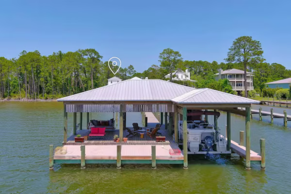 A large covered boathouse with a metal roof sits over the water, featuring a lounge area with outdoor seating and an attached boat slip housing a motorized boat.