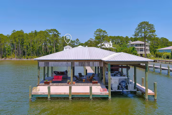 A large covered boathouse with a metal roof sits over the water, featuring a lounge area with outdoor seating and an attached boat slip housing a motorized boat.