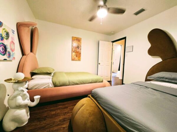Colorful bedroom featuring unique bunny-shaped and bear-shaped beds, a playful sculpture, and vibrant artwork on the wall, highlighting a whimsical design.