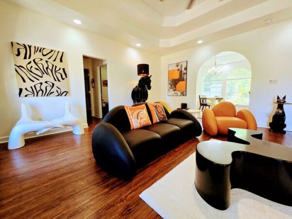 Modern living room featuring a sleek black sofa with vibrant orange accents, unique seating, and contemporary artwork against light walls.