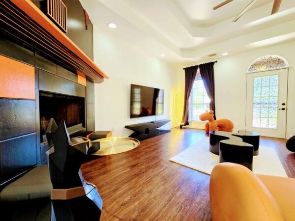 Modern living room featuring a sleek black fireplace, large TV, unique furniture pieces, and natural light streaming through large windows.