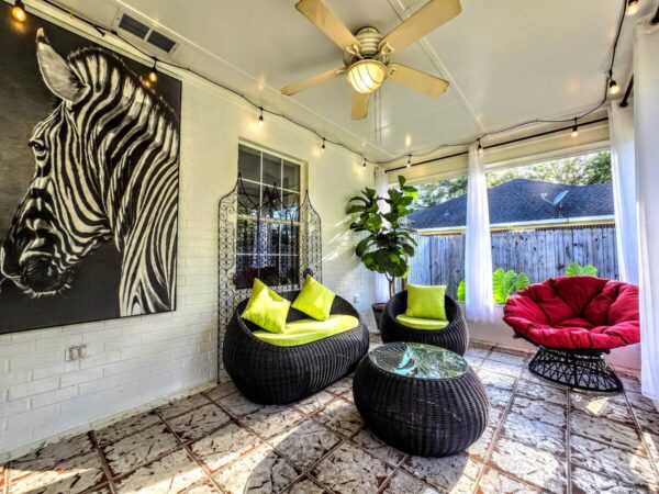 Bright sunroom featuring a zebra portrait, cozy black wicker seating with neon green cushions, and a red papasan chair. Ideal for relaxation.