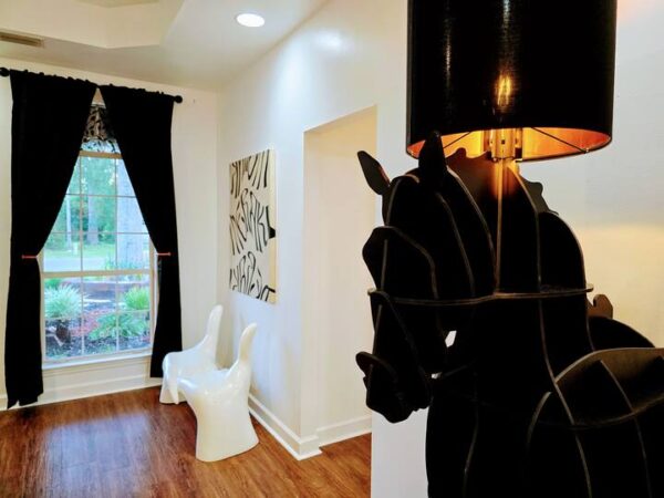 Stylish interior featuring a horse-shaped lamp, modern white chair, and abstract wall art, framed by black curtains and a large window.