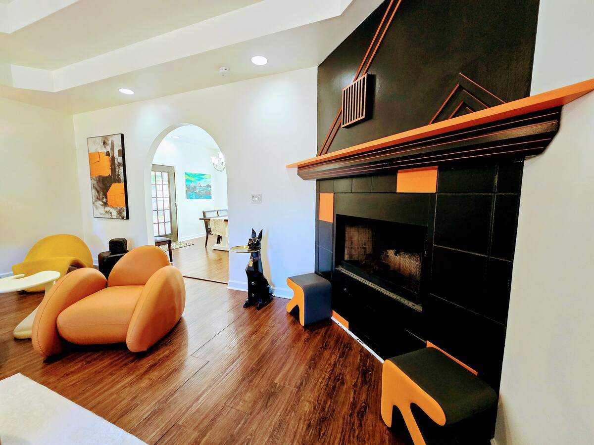 Modern living room featuring a black and orange fireplace, unique furniture, and artwork. The cozy space blends contemporary design elements and warmth.