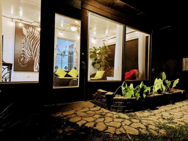 Cozy outdoor space viewed at night, showcasing a well-lit porch with a zebra painting, comfortable seating, and vibrant plants.