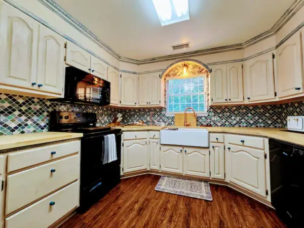 Bright kitchen featuring white cabinets, black appliances, and a farmhouse sink. Colorful tiled backsplash adds visual interest.