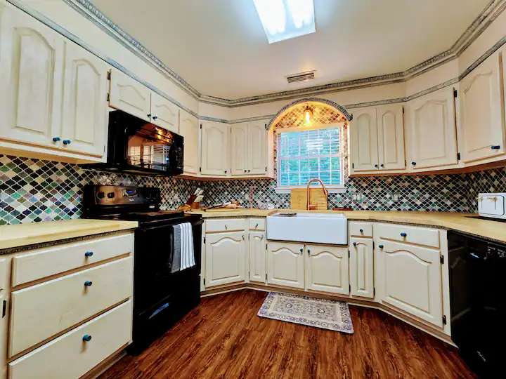 Bright kitchen featuring white cabinets, black appliances, and a farmhouse sink. Colorful tiled backsplash adds visual interest.