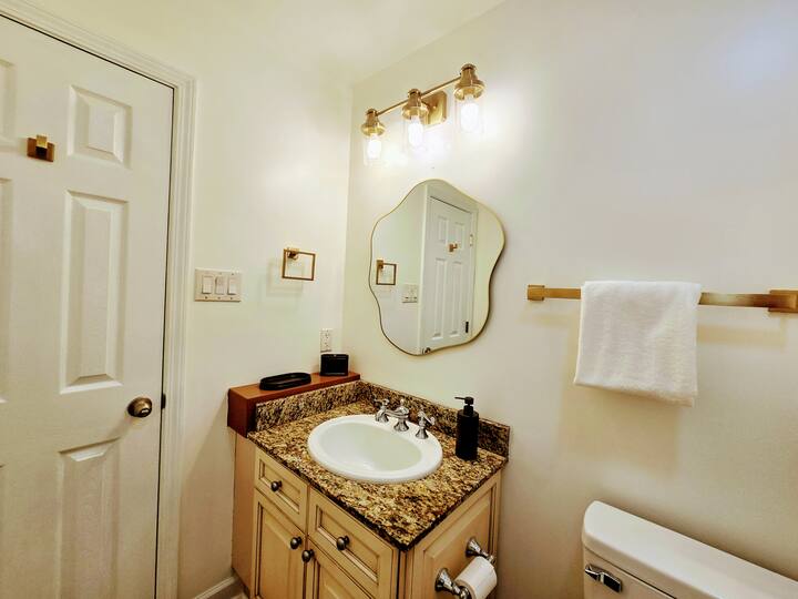 Bright bathroom featuring a granite countertop sink with modern fixtures, a decorative mirror, and stylish lighting above.