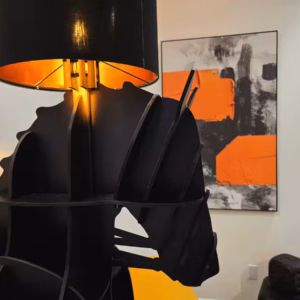 A close-up shot of a black horse-shaped lamp with an orange-lined lampshade, positioned indoors with an abstract orange and black painting on the wall in the background.