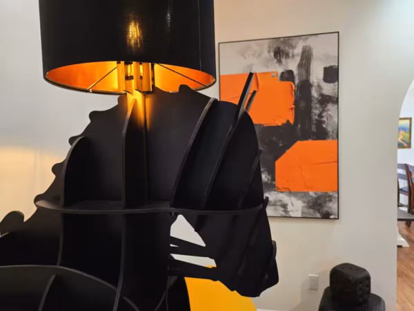 A close-up shot of a black horse-shaped lamp with an orange-lined lampshade, positioned indoors with an abstract orange and black painting on the wall in the background.