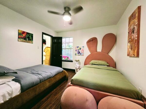 Colorful children's room featuring two beds, one styled as a bunny, with playful artwork on the walls and a window view of a garden.