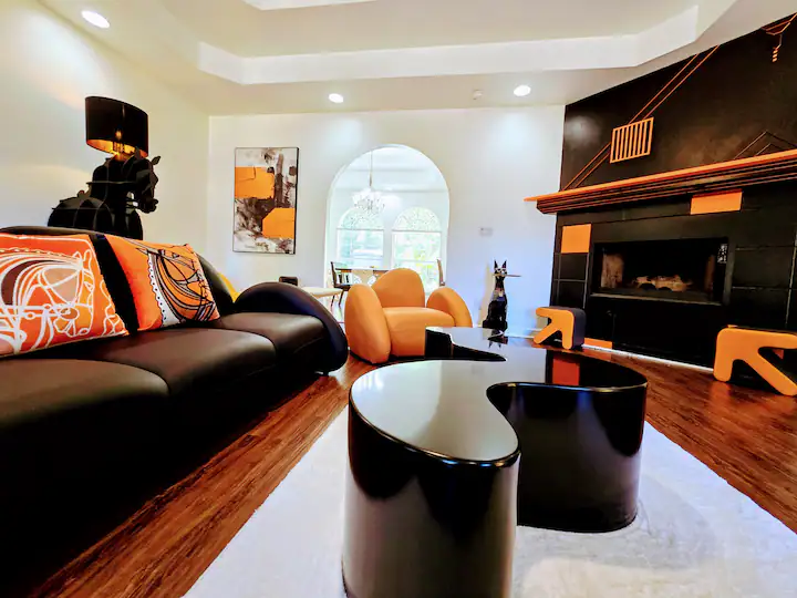 Modern living room featuring a sleek black sofa with orange accents, geometric coffee table, and stylish decor. Bright and inviting atmosphere.