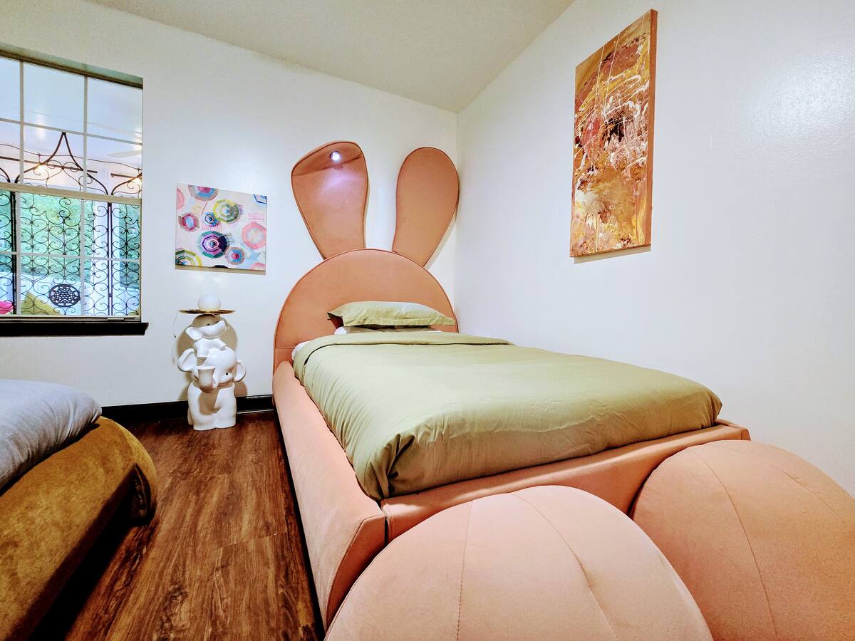 Whimsical bedroom featuring a unique bunny-shaped bed with oversized ears, a modern art piece on the wall, and a playful ceramic sculpture.