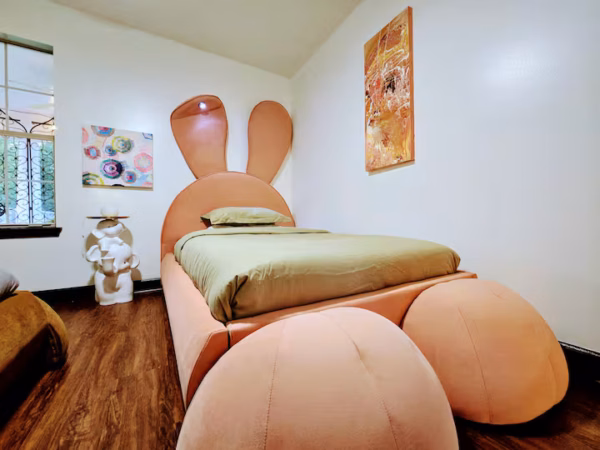 A whimsical bedroom features a custom peach-colored bed designed to look like a cartoon bunny, complete with tall ears on the headboard and large round feet at the foot.