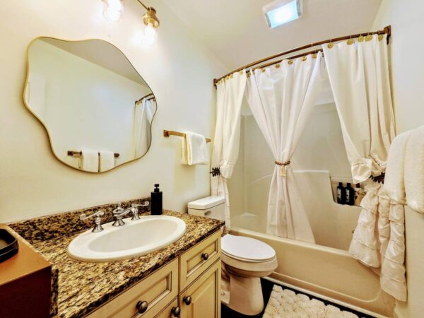Modern bathroom featuring a stylish oval mirror, granite countertop, and a white shower curtain. Clean and inviting atmosphere.