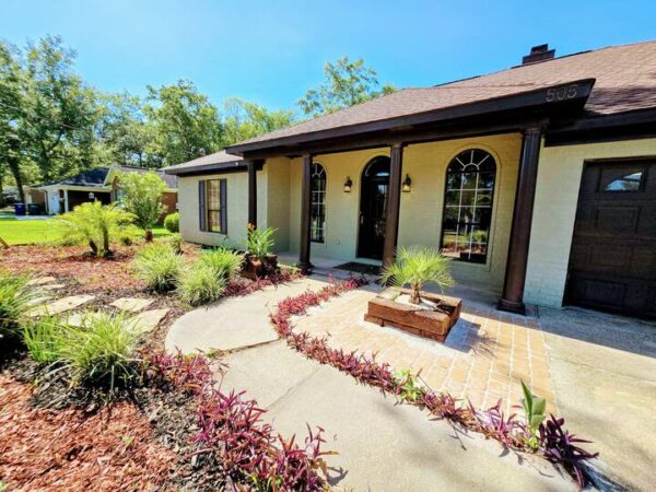 Charming home exterior featuring a well-maintained front garden, pathway, and decorative landscaping under a clear blue sky.